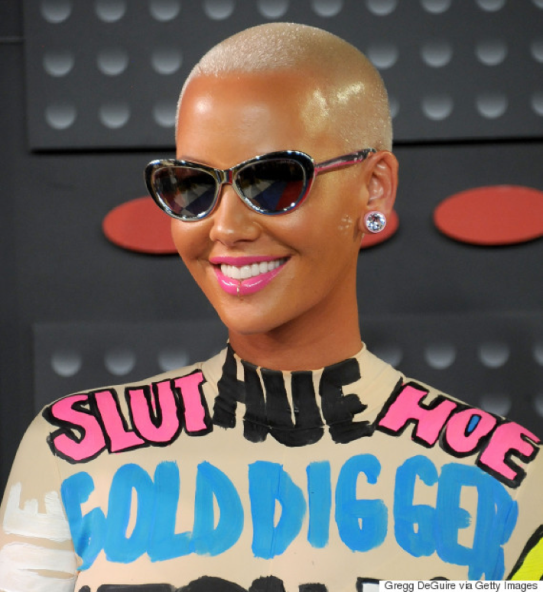 Photo of Amber Rose, smiling with buzz cut blonde hair wearing an outfit that says, "slut, hoe, gold digger."